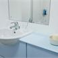 Close up view of sink and mirror in white walled bathroom pod with light blue cupboards