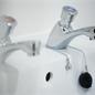 Close up diagonal view of chrome lever basin taps, there's a sink plug wrapped round the far tap
